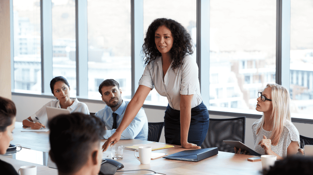 Chief executive officer leading a board meeting, standing at a conference table while presenting strategy to directors in a boardroom.