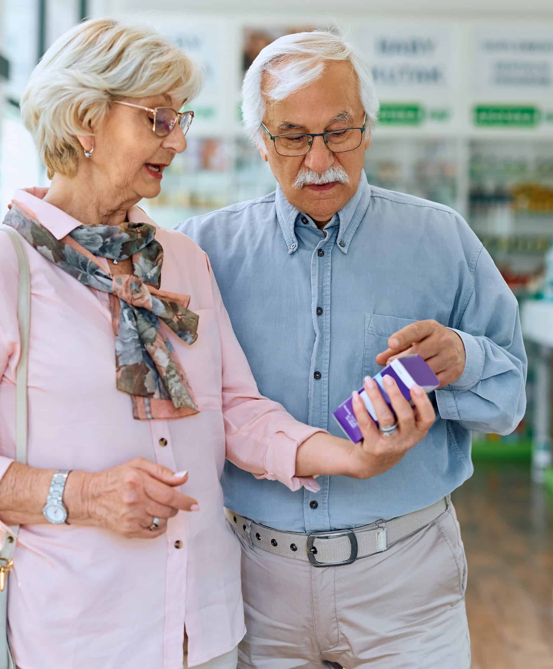 Een ouder echtpaar leest het etiket op een doosje met vrij verkrijgbare medicijnen in een apotheek.