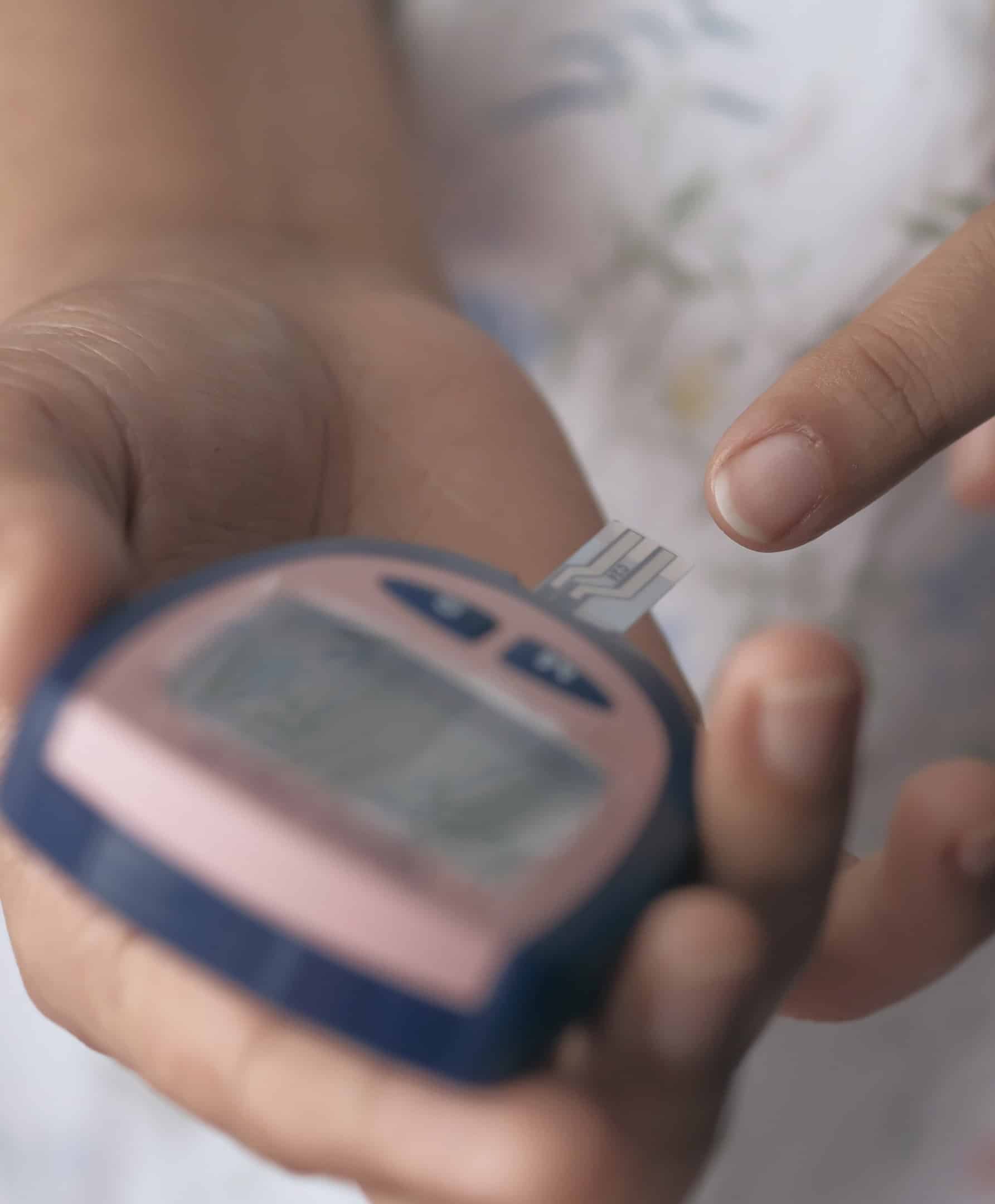 Een persoon plaatst een teststrip in een bloedglucosemeter, een medisch apparaat dat wordt gebruikt bij de behandeling van diabetes.