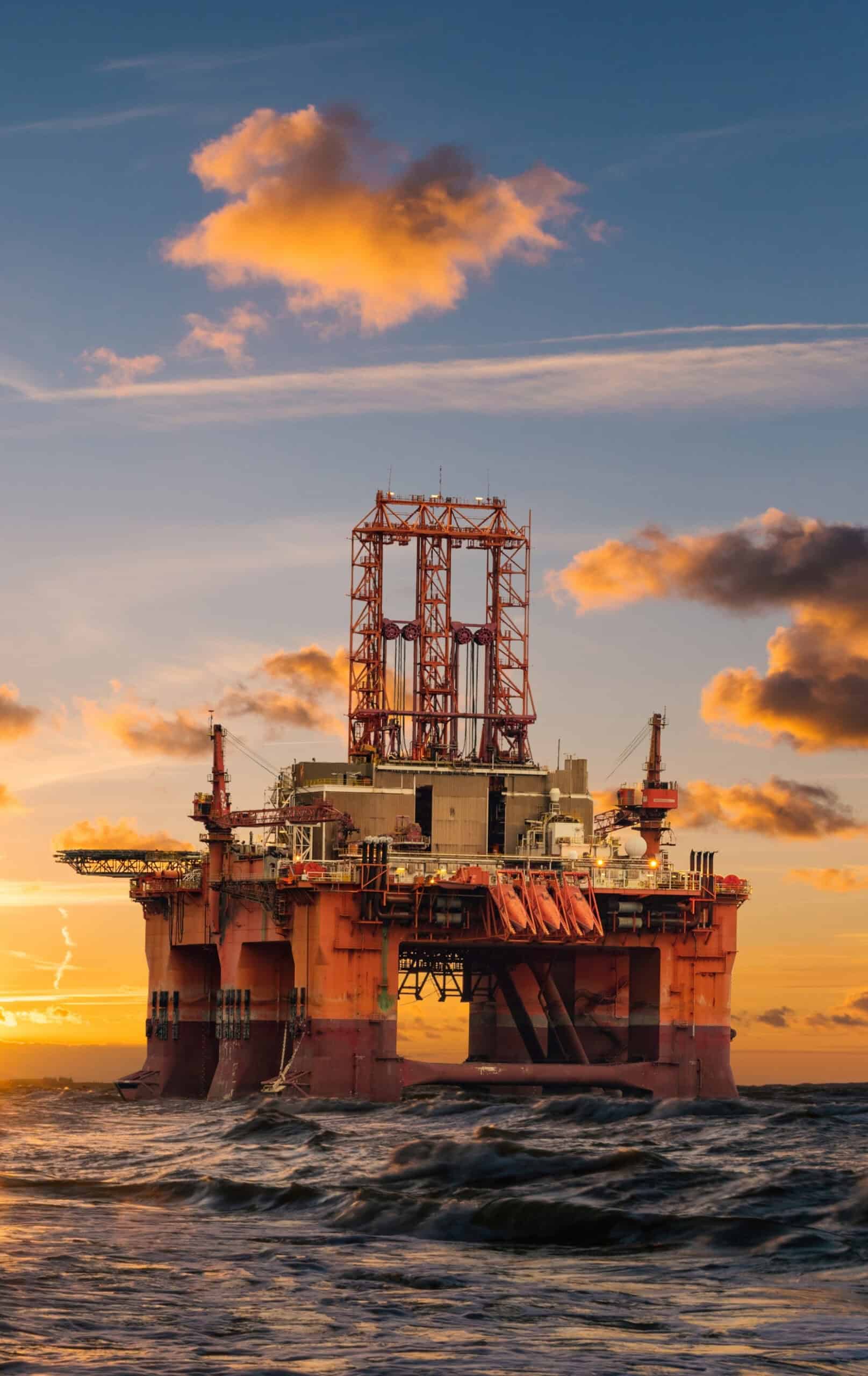 Offshore oil drilling platform at sunset on open seas, representing energy and natural resources executive leadership.