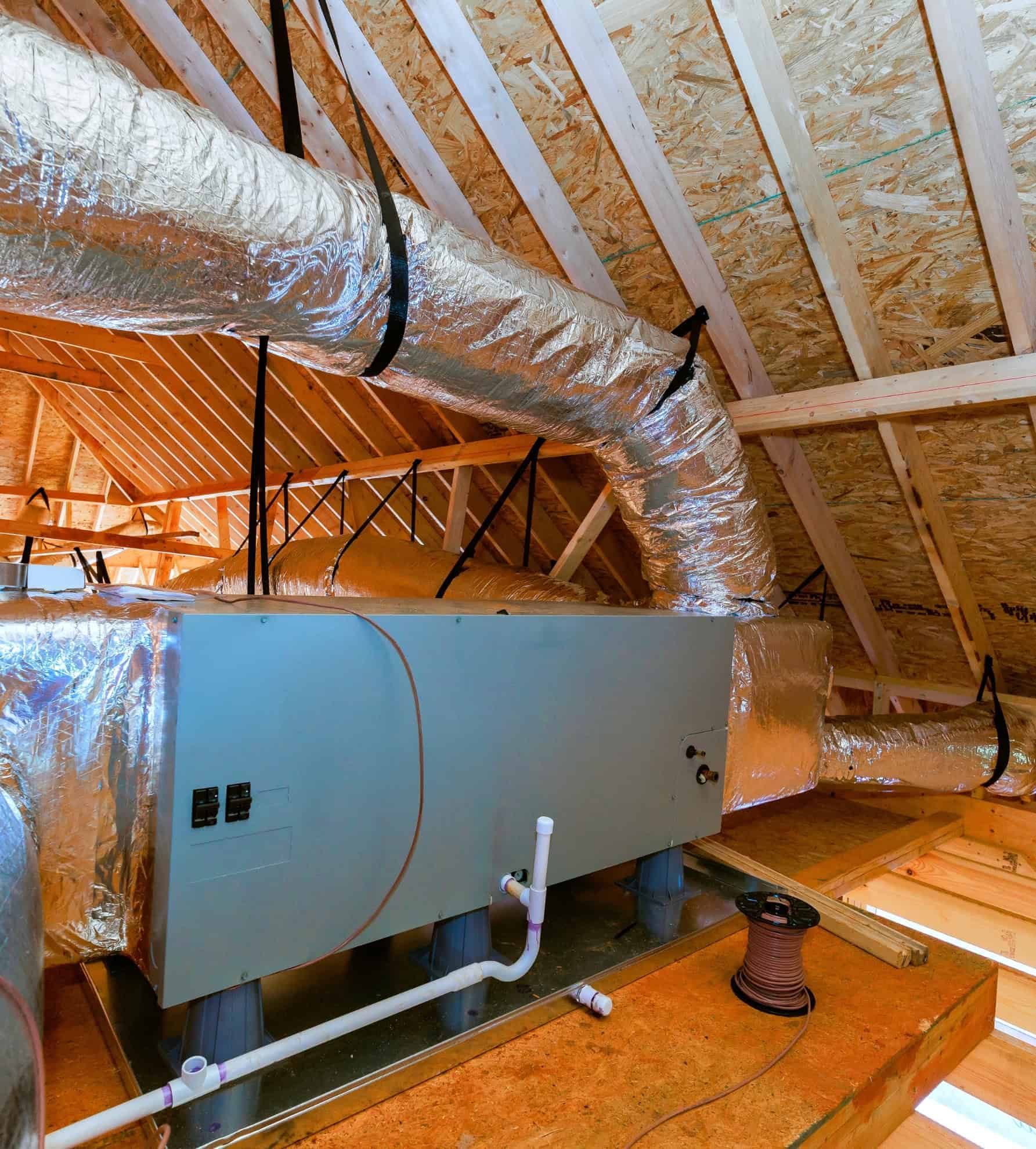 Een HVAC-luchtbehandelingsunit en geïsoleerd leidingwerk geïnstalleerd op een zolder in een nieuwbouwhuis; een installatie van bouwproducten in de HVAC-sector.