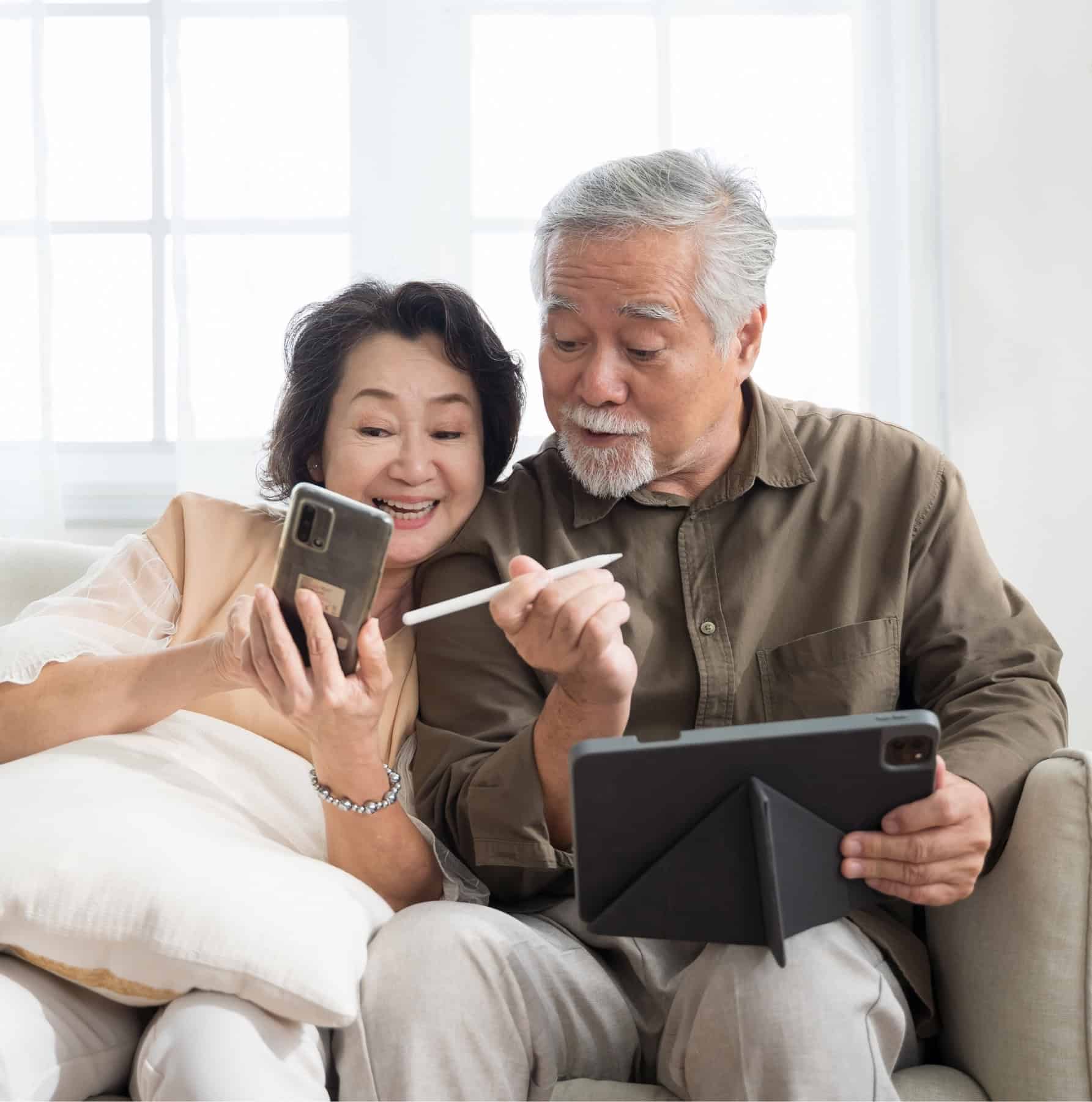 Senior couple using a smartphone and tablet with a stylus, everyday consumer tech in use.