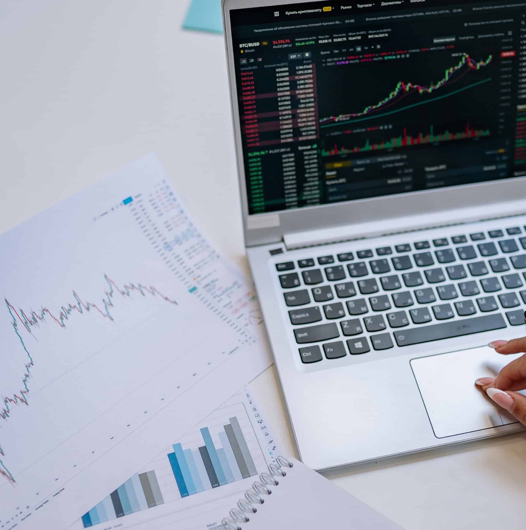 Person reviewing financial data charts on a laptop alongside printed analytics reports in the data analytics industry.