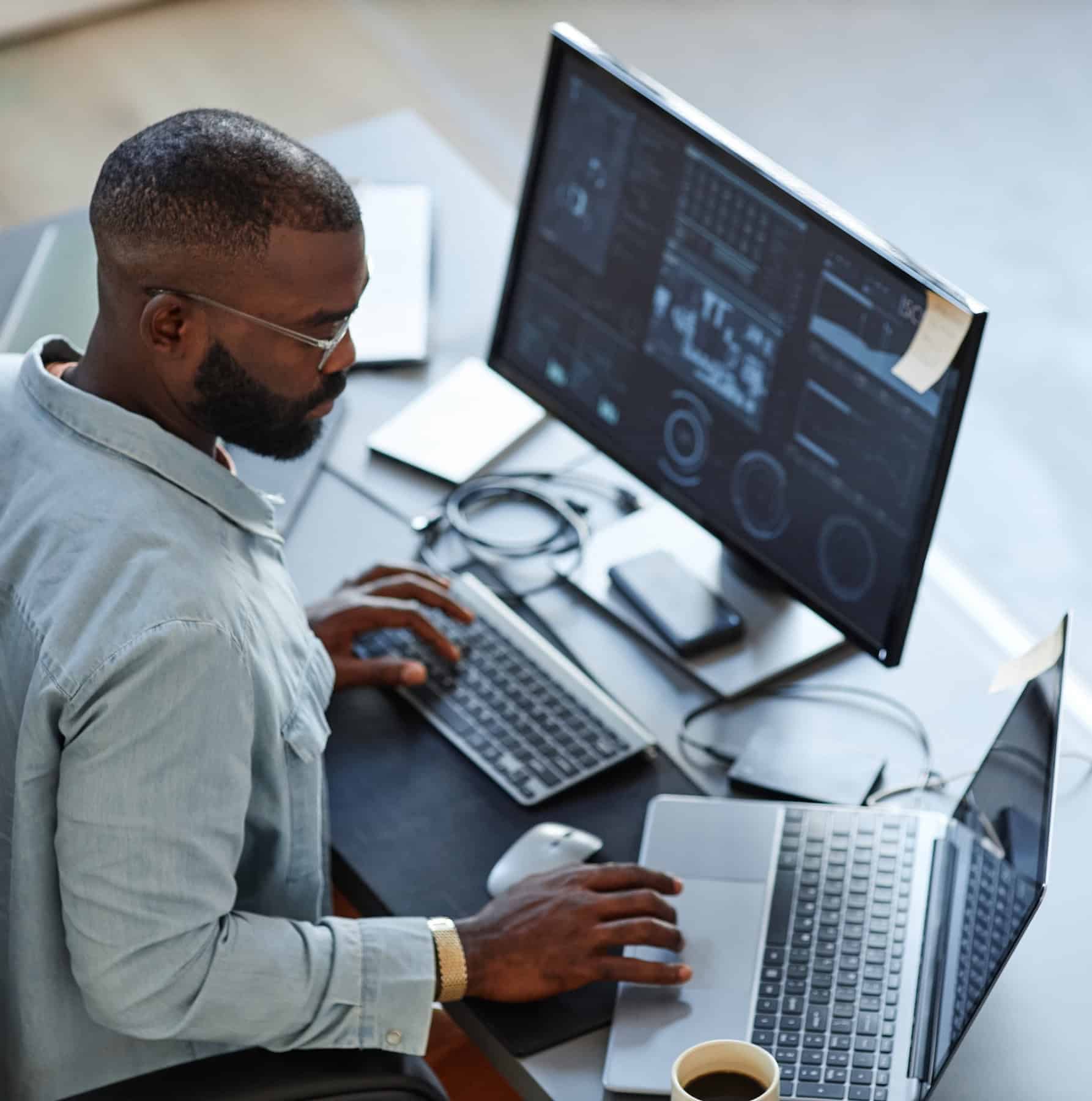 Professional working at a dual-screen setup with a SaaS enterprise software dashboard.
