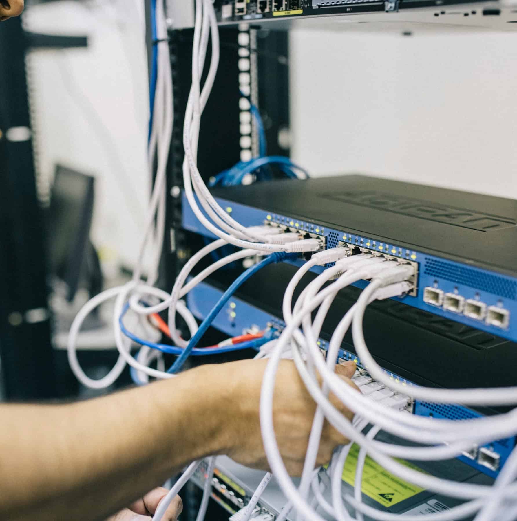 Technician connecting ethernet cables into a network switch in an enterprise hardware and networking environment.