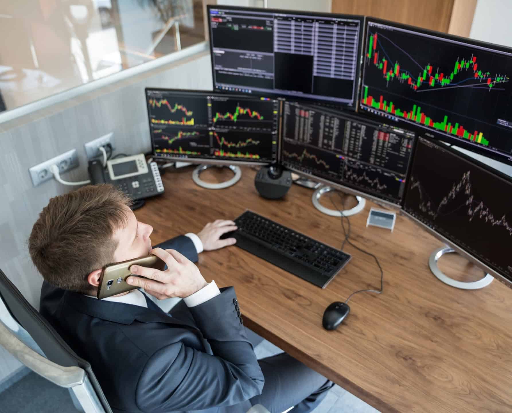 Een hedgefondsmanager zit aan de telefoon en houdt op zijn werkstation meerdere handelsschermen in de gaten.