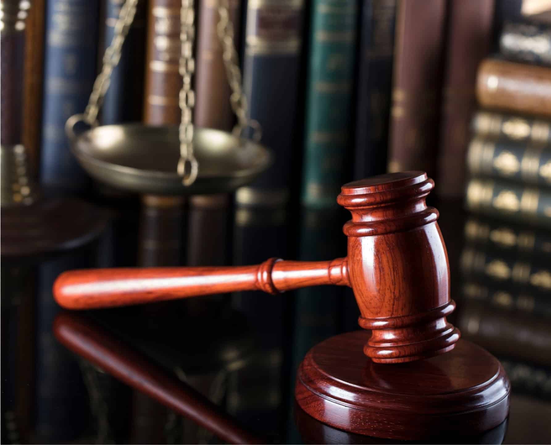 Een houten hamer en weegschaal van justitie tegen een boekenplank in een juridische bibliotheek, als symbool voor juridische dienstverlening.