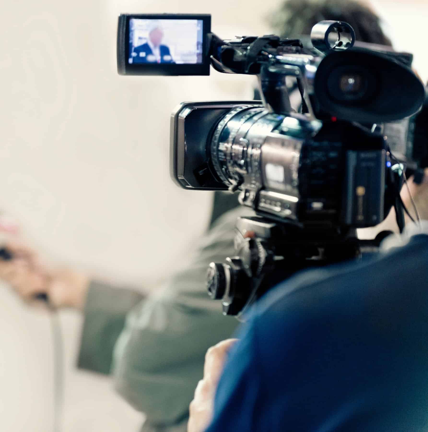 Videographer operating a professional broadcast camera filming a speaker in the digital media industry.