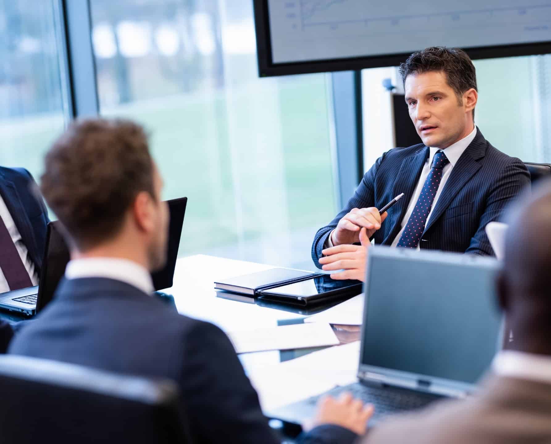 Bestuurders van private equity-bedrijven in een directievergadering met grafieken van beleggingsprestaties op het scherm.