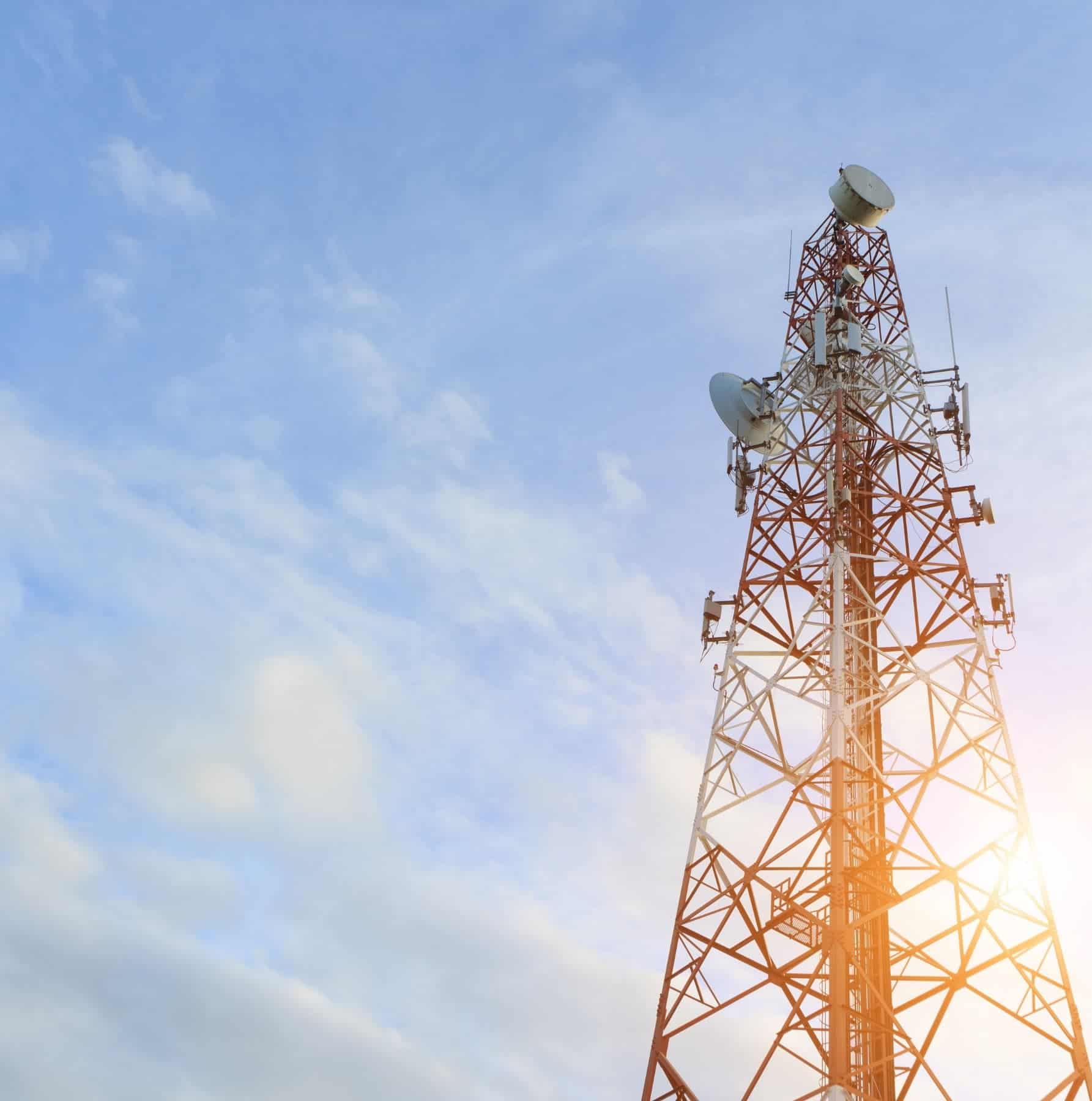 Telecommunications tower with microwave dishes and antenna arrays against a blue sky in the telecom industry.