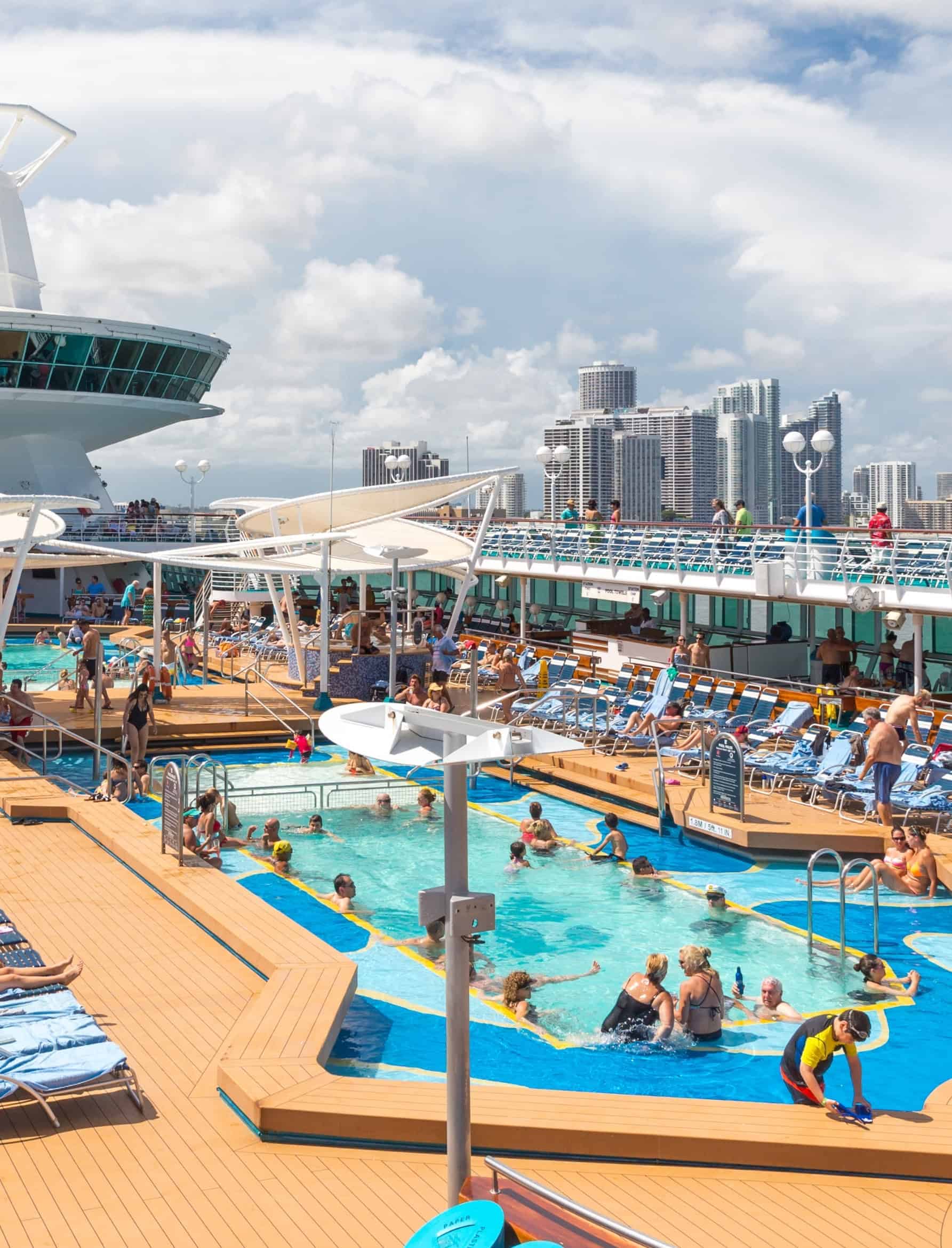 Guests enjoying the pool deck on a cruise ship with a city skyline in the background, in the cruise ship industry.
