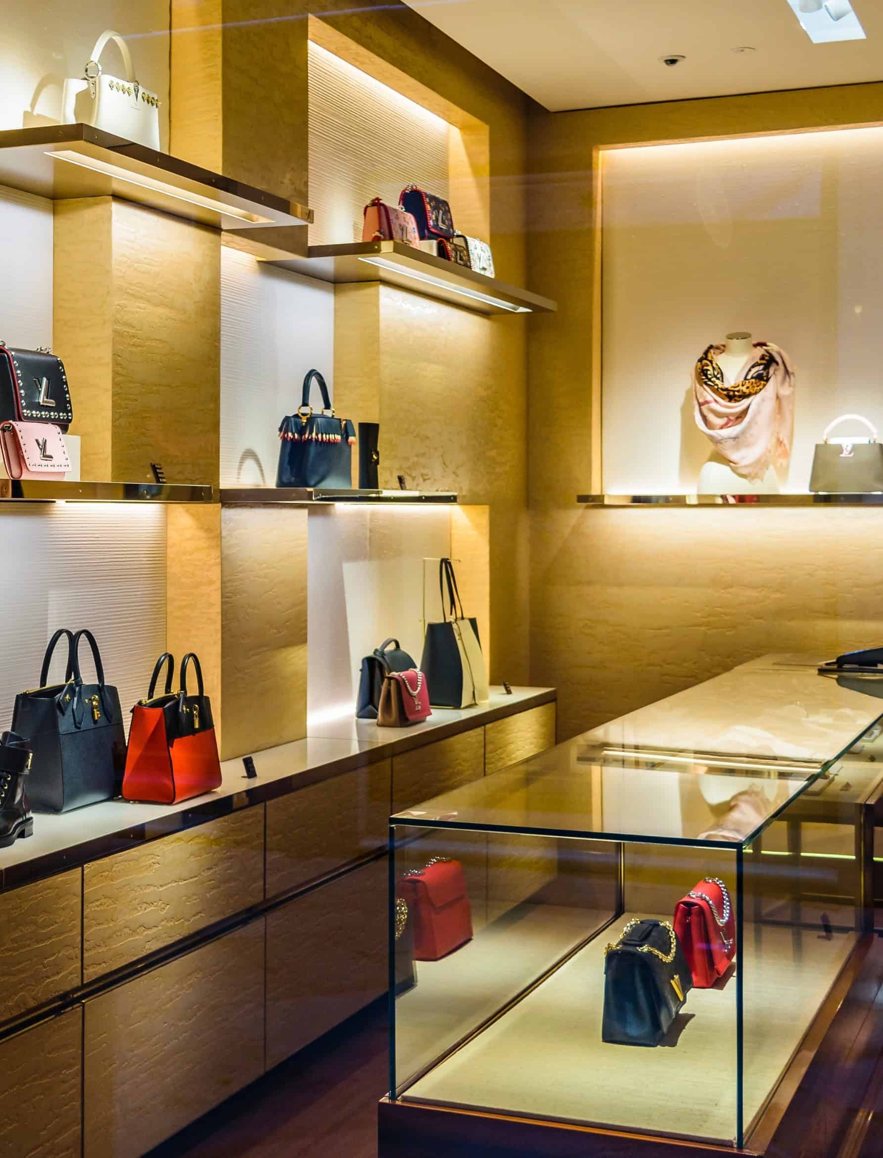 Designer handbags displayed on illuminated shelves in a luxury consumer fashion boutique.
