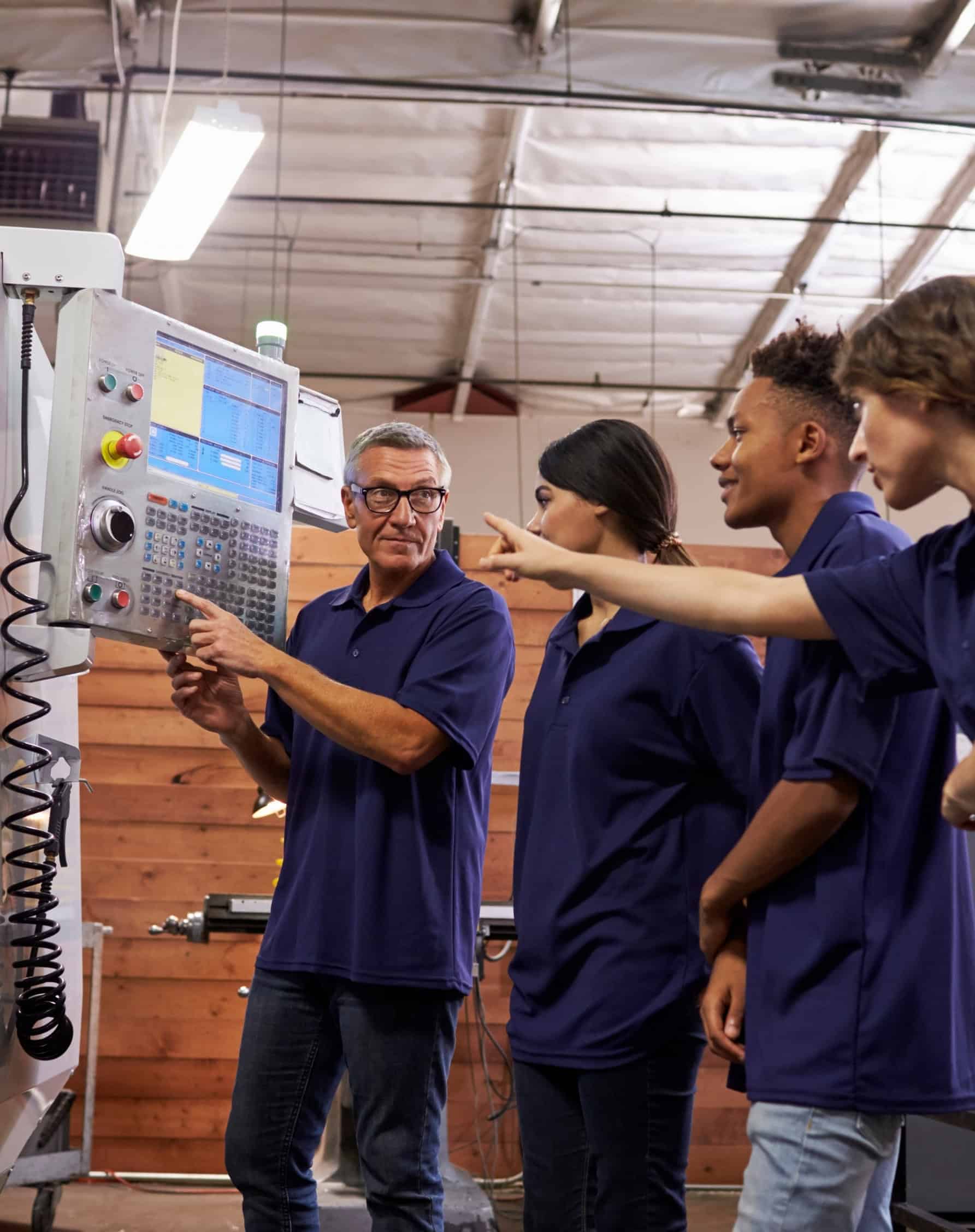 An instructor and apprentices operating industrial machinery at a trade school, representative of the career and workforce education industry.