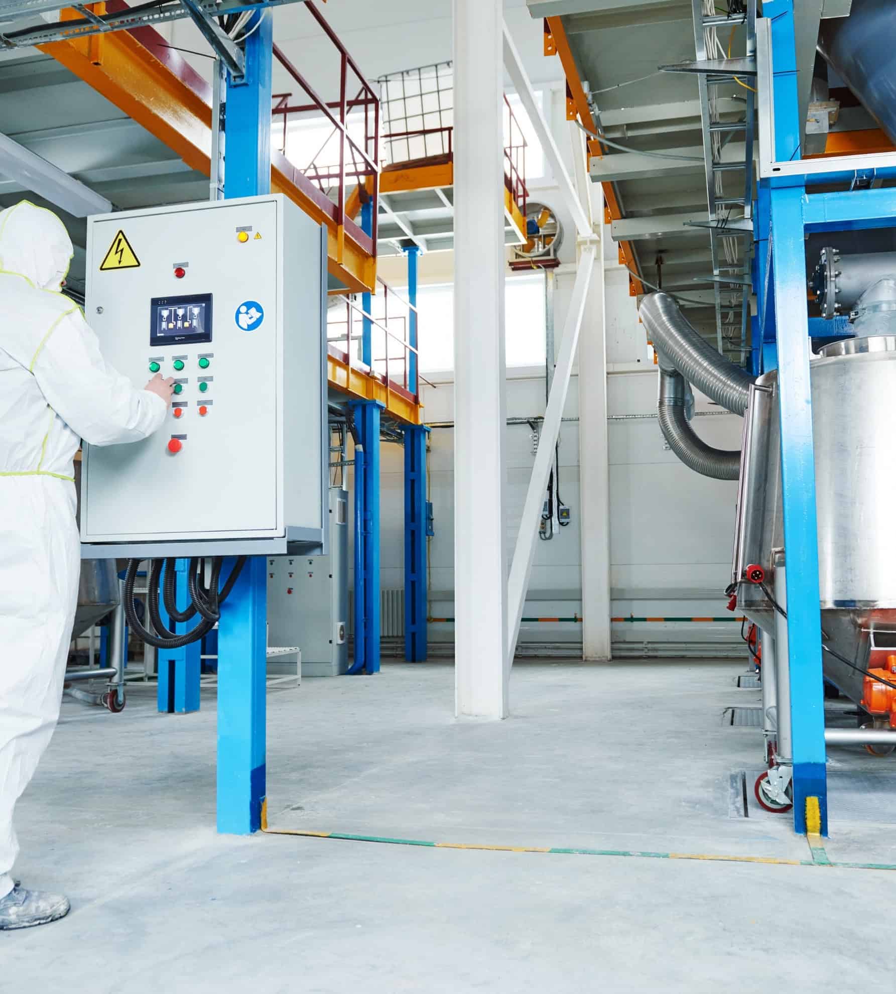 Een werknemer in een beschermend pak bedient een bedieningspaneel in een chemische fabriek, een scène die kenmerkend is voor de chemische industrie.