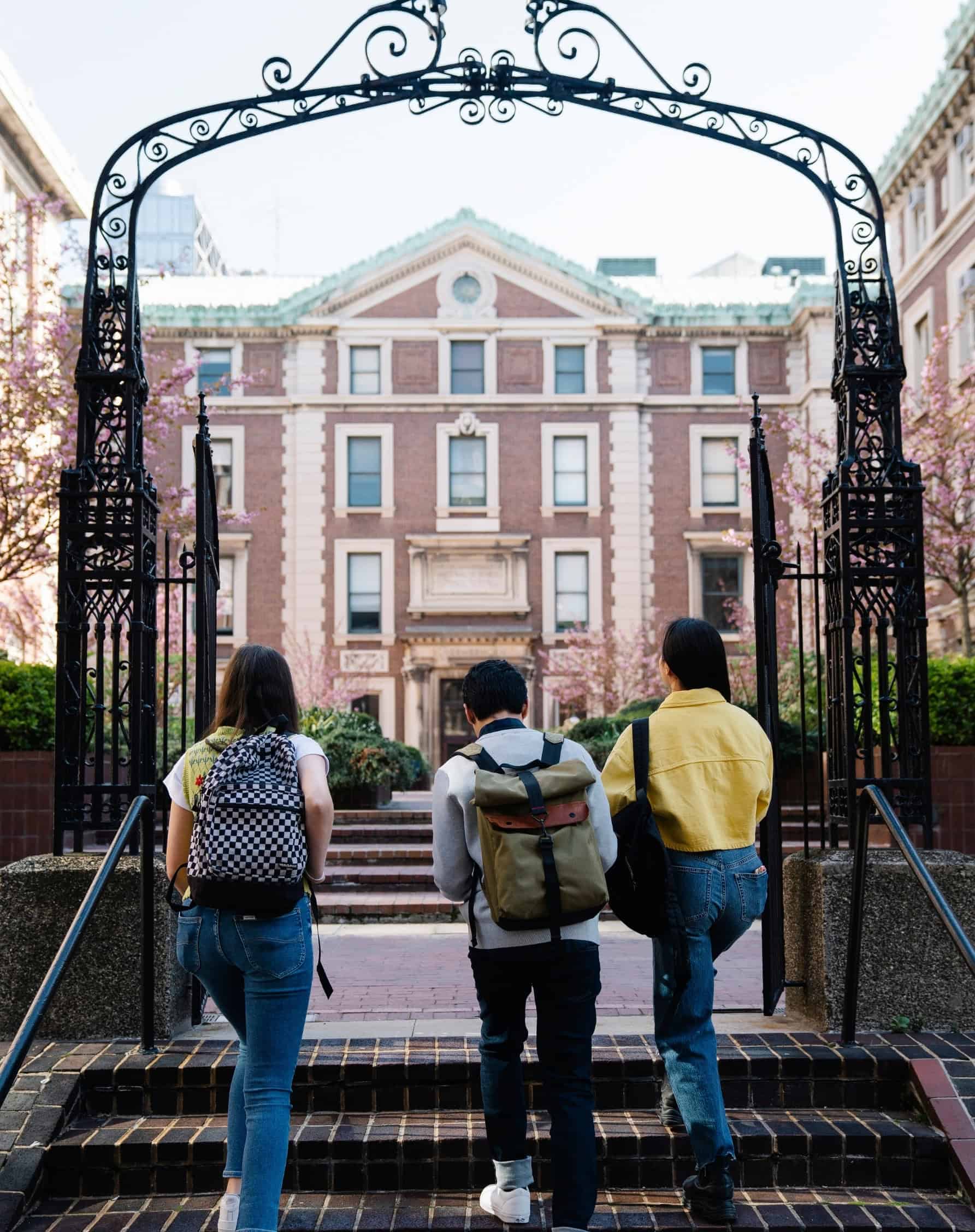 Students walking through ornate iron gates onto a university campus, representing the college and university industry.