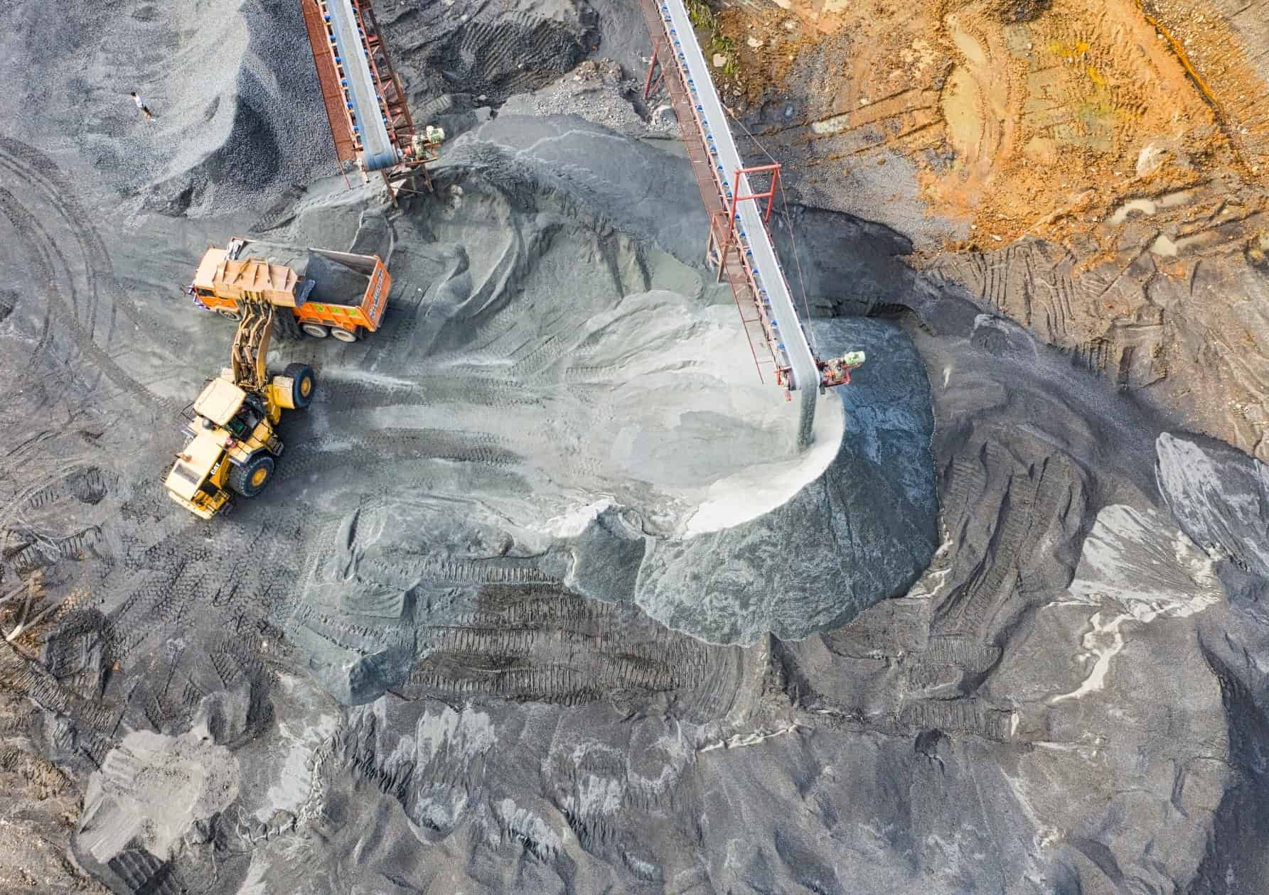 Aerial view of mining and metals operations with heavy equipment and conveyor belt at an open-pit mine.