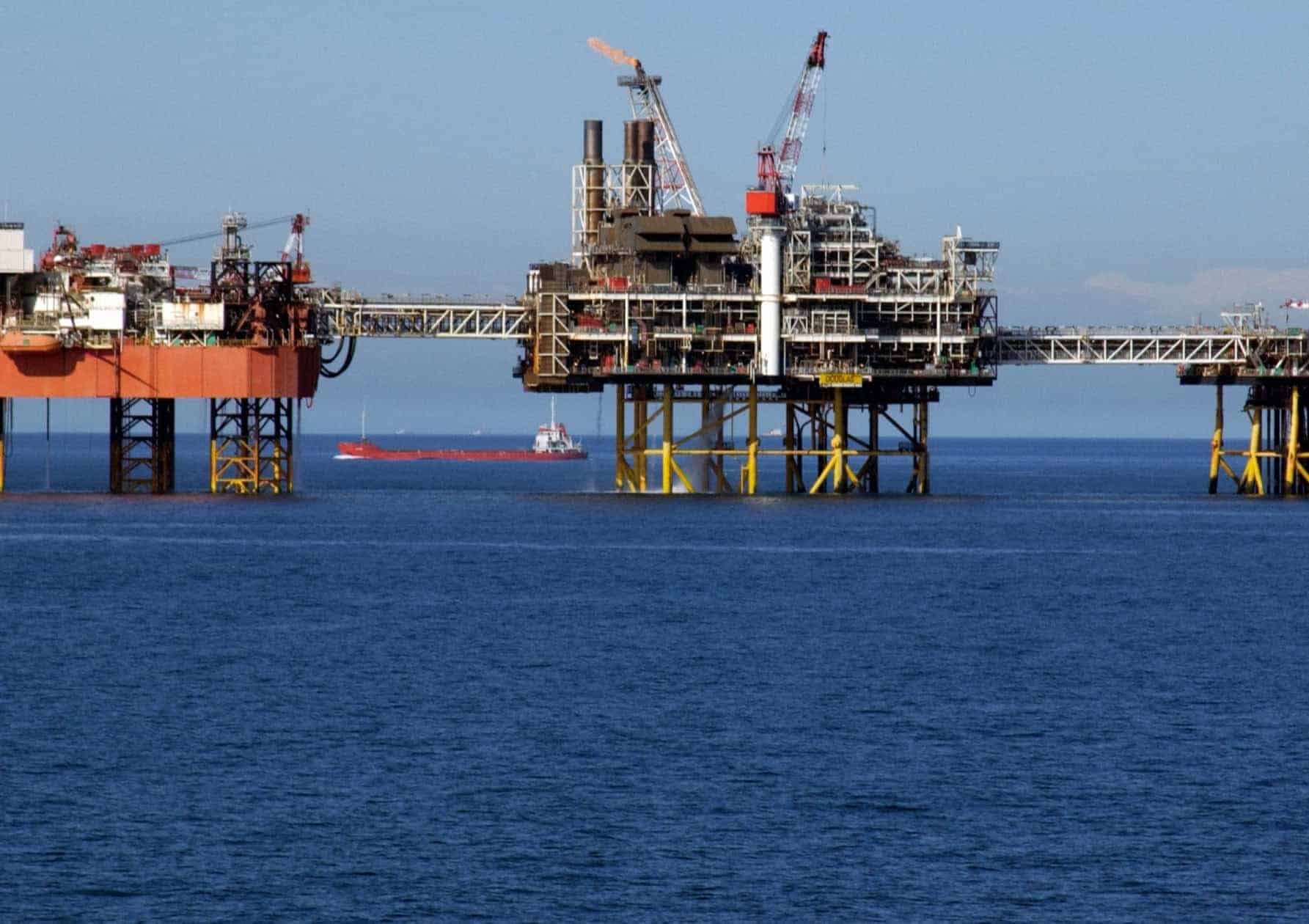 Offshore oil and gas production platforms with an active flare stack and supply vessels on open water.