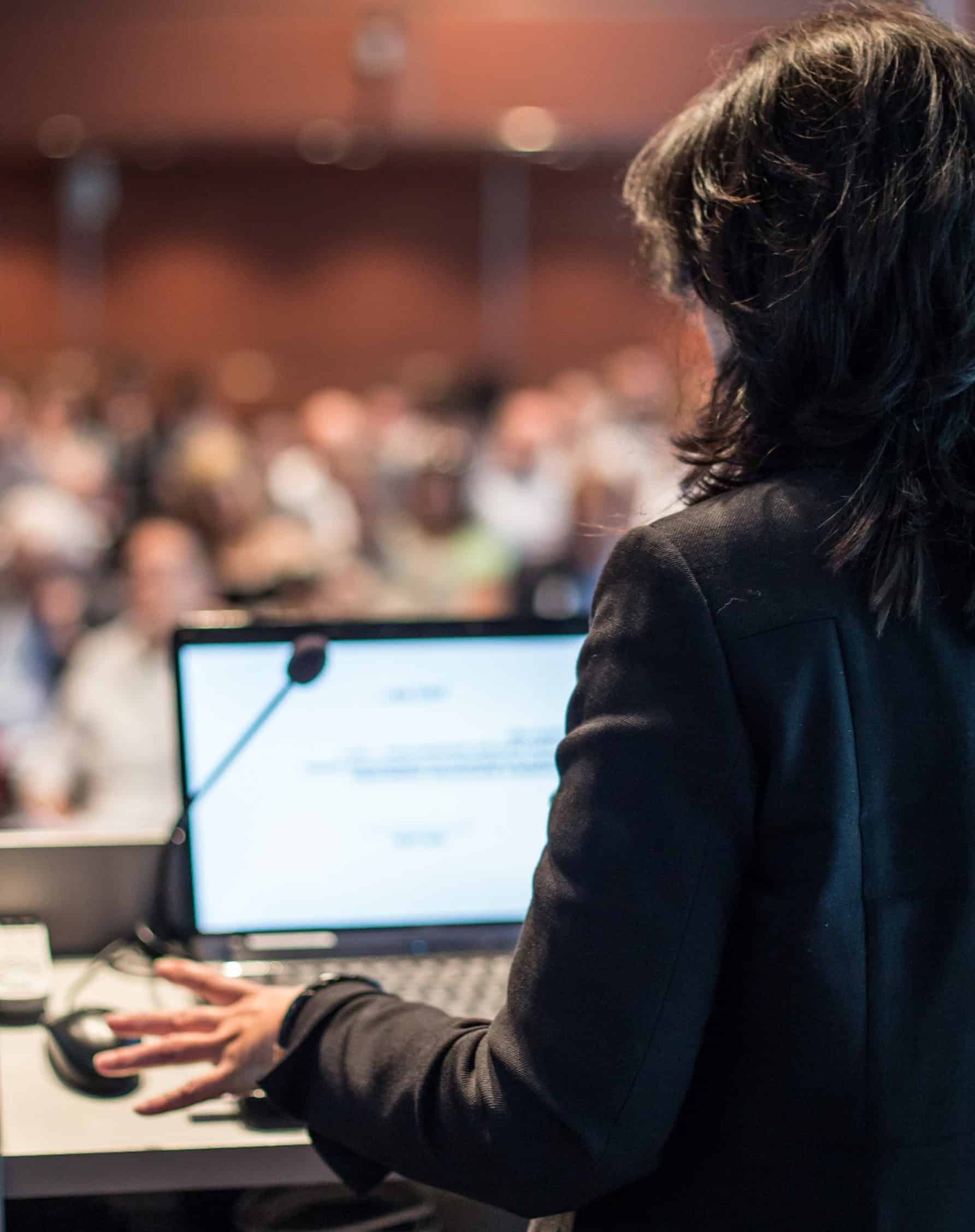 A leader presenting at a podium to a large audience at a philanthropic leadership conference.