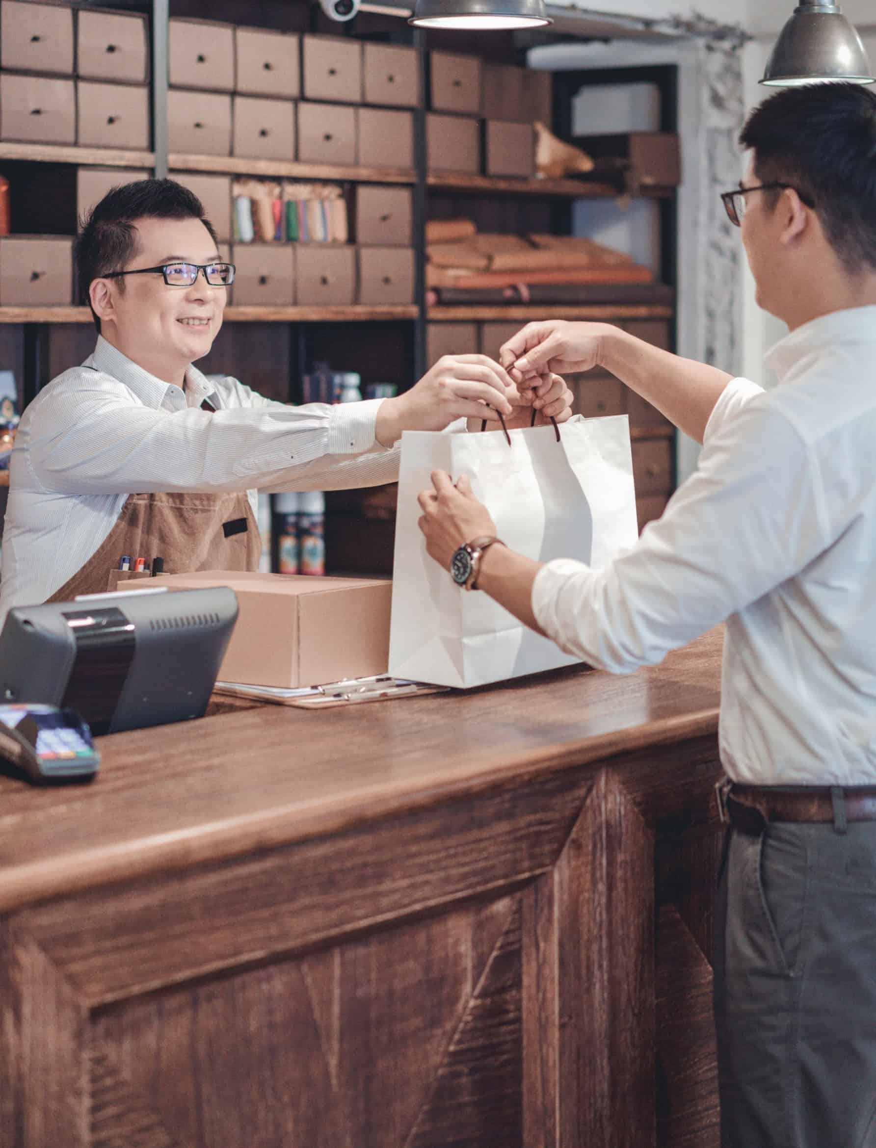 Retail store associate handing a shopping bag to a customer at a boutique checkout counter in the retail industry.