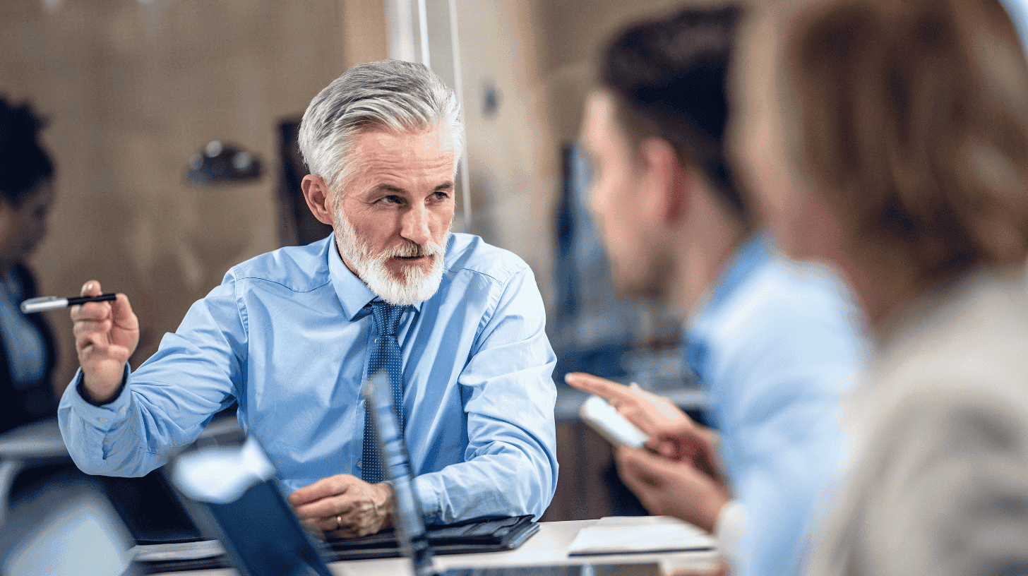 A Chief Strategy Officer gestures with a pen while discussing strategy with colleagues in a meeting.