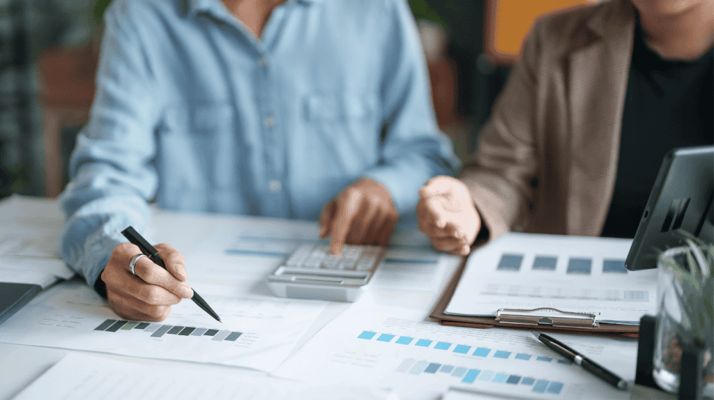 Two executives compare printed charts and reports at a desk while discussing revenue leadership.
