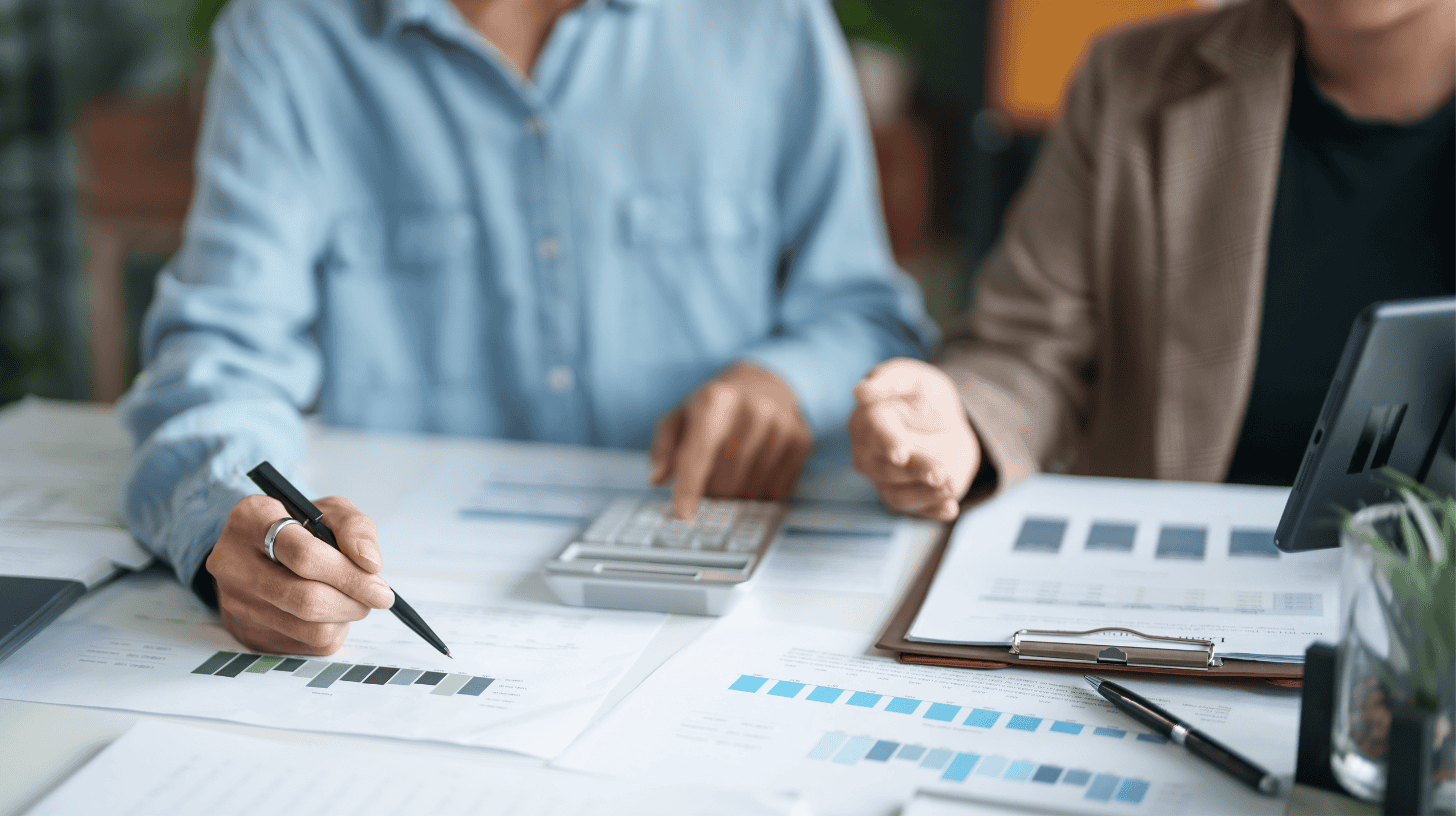 Two executives compare printed charts and reports at a desk while discussing revenue leadership.